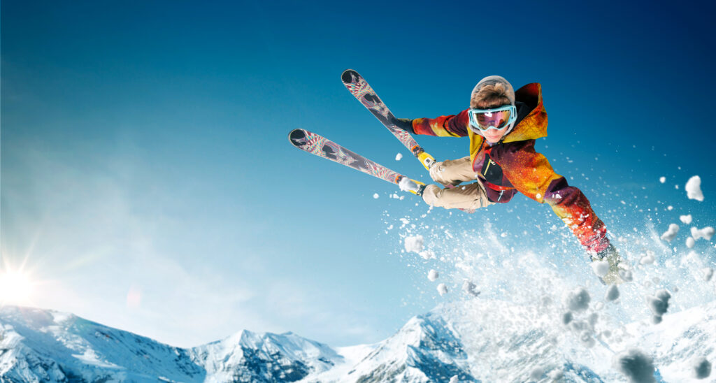 person with orange and colorful ski suit with freestyle skis doing a jump